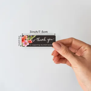 Detail view of rectangular thank you sticker with floral design, showing size in hand.