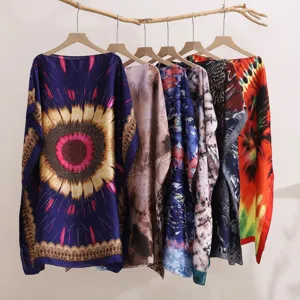 Close-up of multiple colorful printed beach kaftans and shawls hanging on wooden branch.
