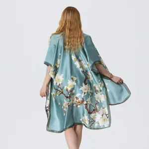 Detail view of a turquoise floral kimono cape with white magnolia print and green trim.