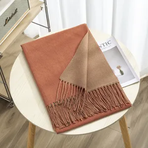 Close-up of a cozy double-sided color-block winter scarf with fringe detail on wooden table.
