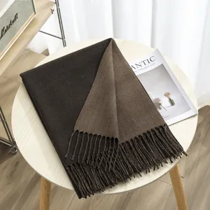 Close-up detail of the reversible two-tone winter scarf with delicate fringes on wooden table.