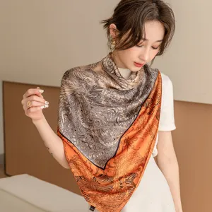 Detailed view of the elegant orange and black printed square silk scarf worn by model.
