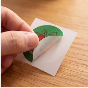 Detail shot of Christmas round sealing sticker being peeled off backing, festive holiday DIY decor.