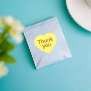 Heart shaped thank you sticker detail on blue background paper bag close up shot