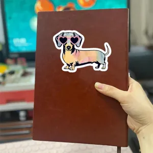 Gros plan détaillé d'un sticker mignon teckel dessin animé avec lunettes soleil cœur sur carnet.