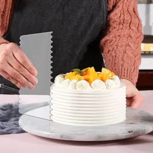 Detail view of a clear cake scraper being used to smooth and decorate a layered cream cake.