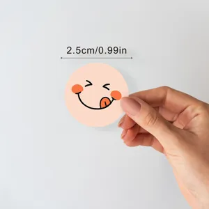 Detail view of round colorful smiley face reward sticker being peeled by hand, size 2.5cm.