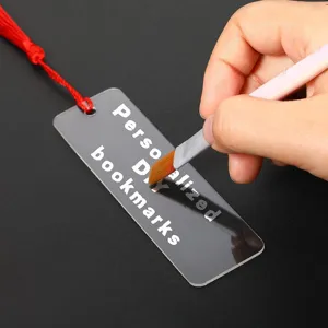 Marcapáginas de acrílico transparente con borla roja y texto DIY para manualidades.