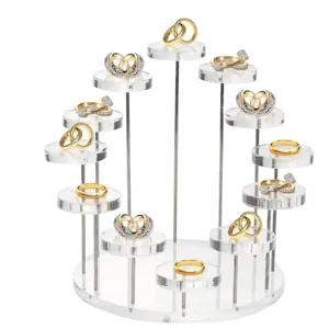 Détail d'un support de bague en acrylique transparent avec plusieurs bagues dorées.