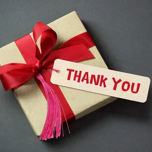 Caja de regalo de papel kraft con cinta roja, borla rosa y etiqueta de agradecimiento.