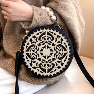 Round wooden hollow carved handbag detail featuring elegant pearl handle and black strap.