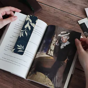 Close-up detail of wooden bookmark with green tassel and botanical leaf pattern on book.
