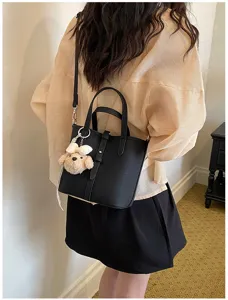 Detailansicht der eleganten schwarzen Beuteltasche mit Henkel und süßem Plüschtier-Anhänger.