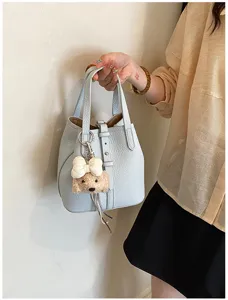 Schicke hellblaue Leder-Eimer-Tasche mit süßem Plüschwelpen-Anhänger, stilvolles Detail.