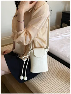 Elegante weiße Mini Umhängetasche für Damen, stilvolle Handytasche mit niedlichen hängenden Bällen.