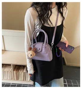 Chic purple bowling bag for women, stylish crossbody handbag with cute bear pendant and top handles.