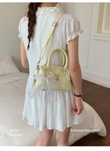 Detail view of the elegant light yellow handbag featuring a sweet bow and lace ribbon accent.