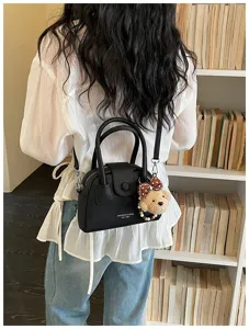 Black leather bowling shoulder bag detail featuring cute bear charm and metal hardware.