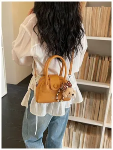 Women's brown bowling handbag with crossbody strap and cute teddy bear pendant detail.