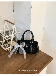 Detailed view of black handbag featuring white lace bow and heart charm in lifestyle scene.
