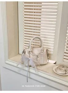 Elegant white women handbag detail shot, featuring bowknot and strap design on windowsill.