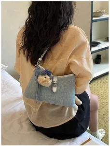 Gedetailleerd overzicht van lichtblauwe denim schoudertas met schattige berenhanger en slotje.
