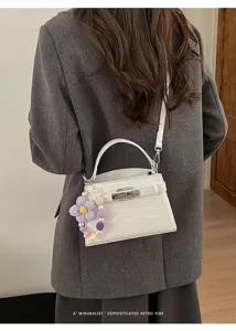 Detailed view of white crocodile pattern shoulder bag with cute knitted flower charm.