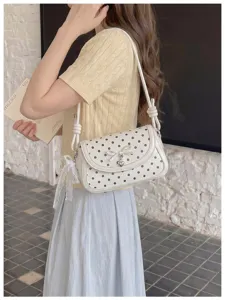 Detail view of the elegant white polka dot shoulder bag with cute bow and heart pendant.