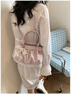 Detailed view of pink pleated crossbody bag with elegant pearl bow charm and soft leather.