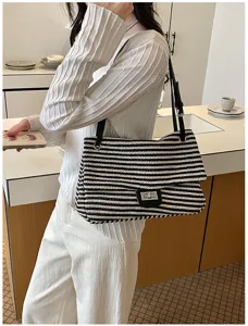 Vista detallada de un elegante bolso de hombro de paja tejida a rayas en blanco y negro con correa.