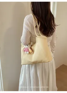 Detailed view of minimalist yellow shoulder tote bag with cute knitted doll pendant.