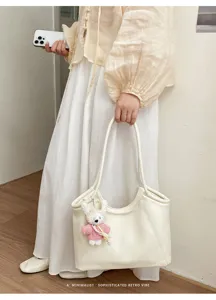 Close-up detail shot of the elegant white shoulder tote bag with a cute plush bear charm.
