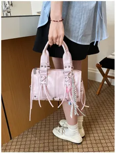 Detail shot of the pink leather handbag featuring stylish tassels, metal studs, and charms.