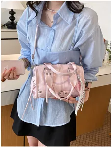Detailed shot of pink glossy leather Boston handbag with metal studs and cute side tassel charms.