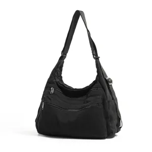 Detalle de bolso cruzado de lona negra con múltiples bolsillos con cremallera y correa ajustable.