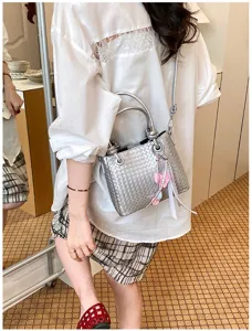 Detail shot of a trendy silver woven bucket bag with metal handles and shoulder strap.