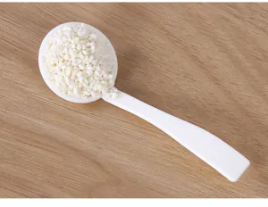 Close-up detail shot of a white plastic spoon filled with seasoning powder on wooden table.