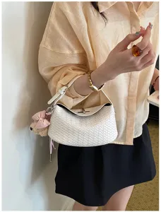 Close-up of a stylish white woven dumpling handbag with unique texture and cute bear charm.