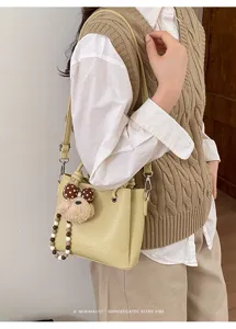 Trendy yellow bucket bag with cute bear pendant and bead strap detail for women.