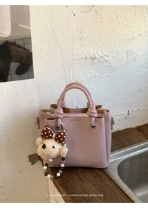 Detailed view of the pink faux leather bucket bag with cute bear charm and twisted handles.