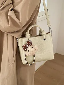 Chic beige leather bucket bag with cute plush bear pendant and stylish crossbody strap.