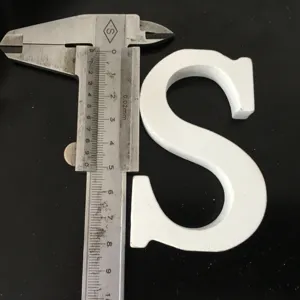 Close-up detail shot of a white wooden letter S being measured with a metal caliper tool.