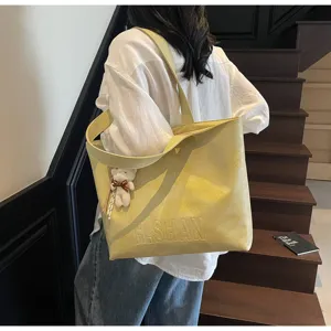 Detail view of a large yellow leather tote shoulder bag with cute bear pendant for daily commuting.