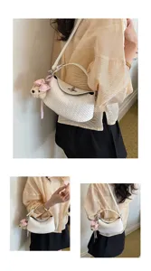 Detail view of the stylish elegant white woven dumpling crossbody bag with cute charm.