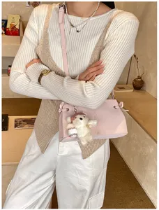 Detailed view of pink shoulder bag with cute bear pendant, matching chic knitwear outfit.