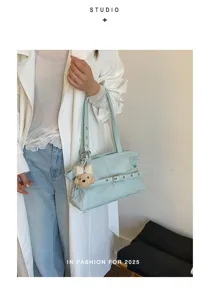 Detail view of a stylish light blue shoulder bag with a cute plush charm and belt accent.