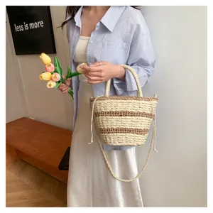 Vue détail du sac seau rétro en paille tissée avec motif rayé et bandoulière de transport chic.