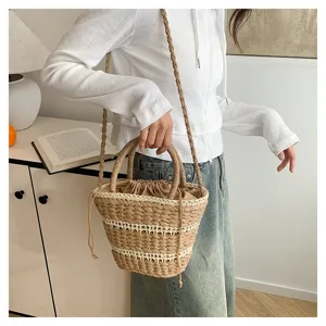 Vue détaillée du sac seau en paille tissée avec bandes contrastées et cordon.