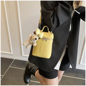 Detail shot of yellow mini leather crossbody bag with cute puppy pendant and double zipper closure.