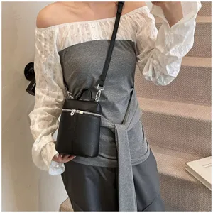 Close-up detail shot of a black textured mini bucket shoulder and crossbody bag worn.